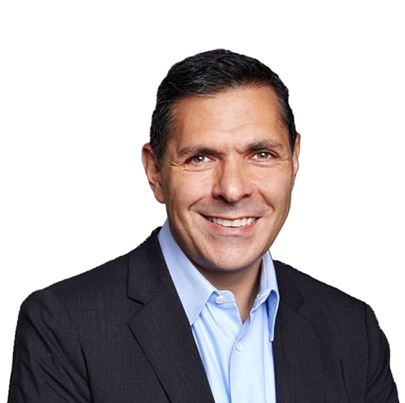 A smiling man wearing a dark suit and light blue shirt, photographed against a plain white background.