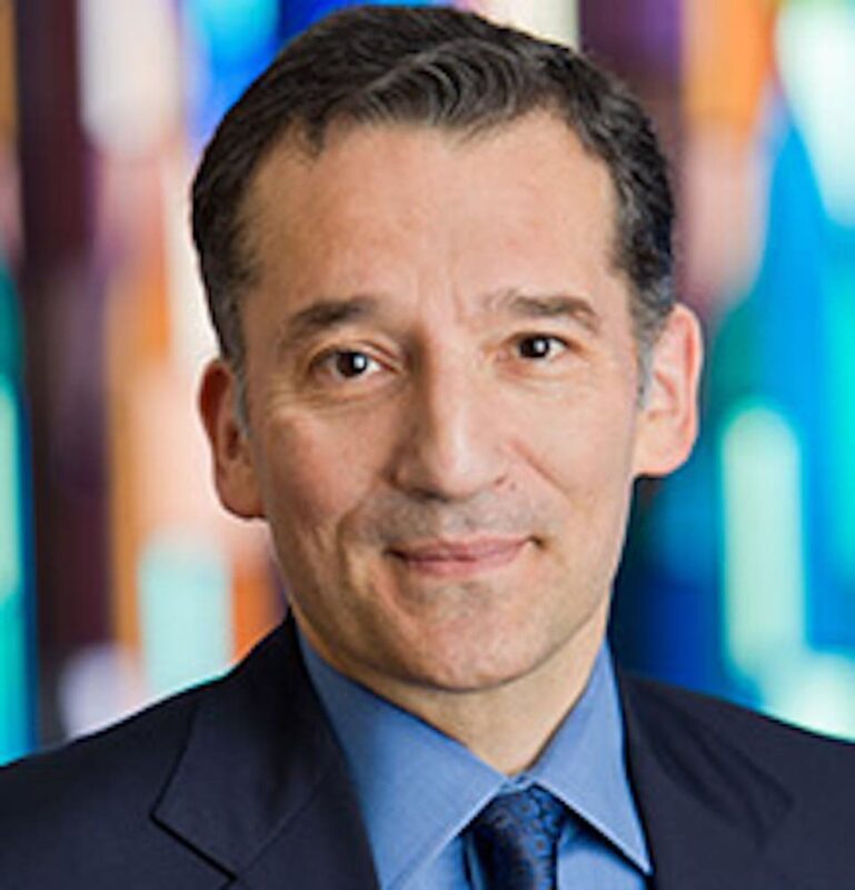 Man in a suit and tie smiling with a colorful, blurred background.