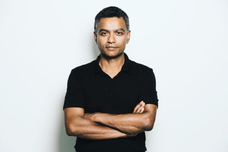 Man in a black shirt standing with arms crossed against a plain white background.