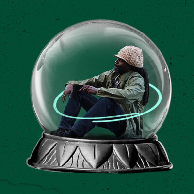 Person wearing a hat and jacket sits inside a large snow globe on a green background.