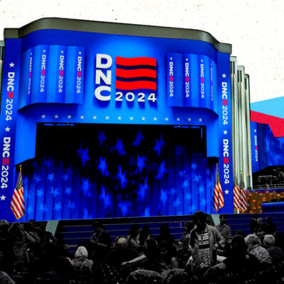 Stage setup for the 2024 Democratic National Convention with a large screen displaying "DNC 2024" and people seated in the foreground.