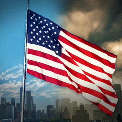 U.S. flag waving against a city skyline with a partly cloudy sky and a shadowed, dramatic background.