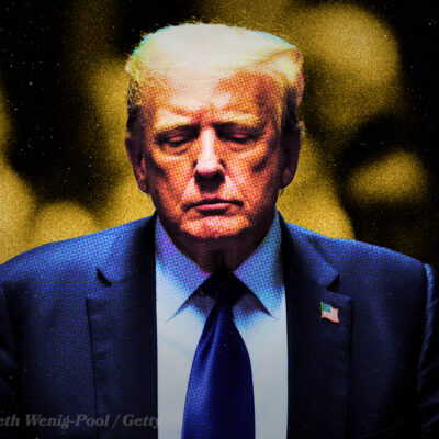 A solemn man in a suit with an American flag pin, set against a dark, blurred background.