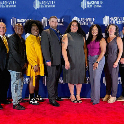 A group of people posing on a red carpet at the Nashville Film Festival, with a blue backdrop featuring the event's logo.