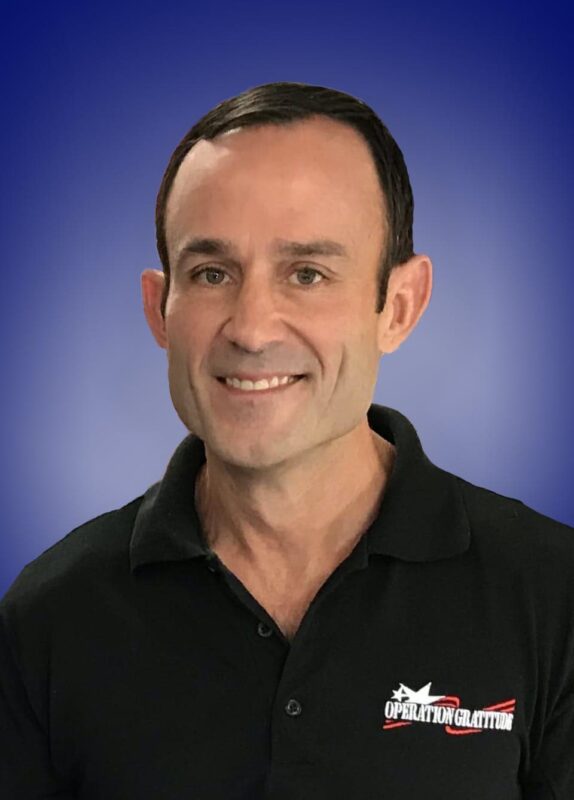 Smiling person in a black "Operation Gratitude" polo shirt with a blue gradient background.