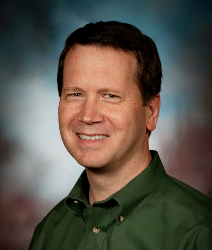 Smiling person in a green shirt against a blurred background.