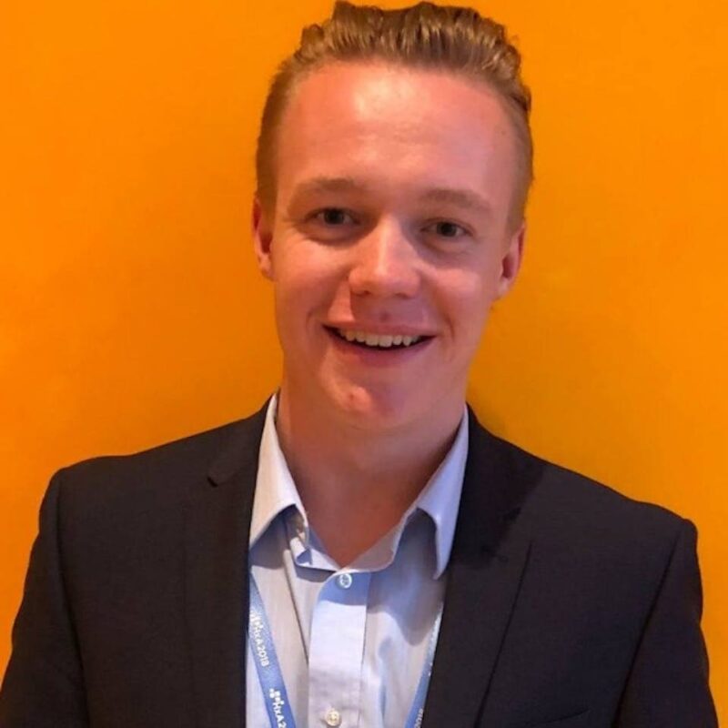 Smiling person in a suit against a bright yellow background.