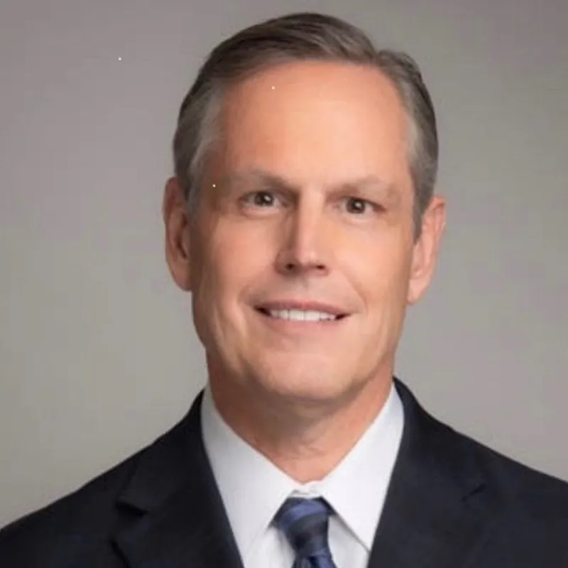 A man in a suit and tie smiling against a plain background.