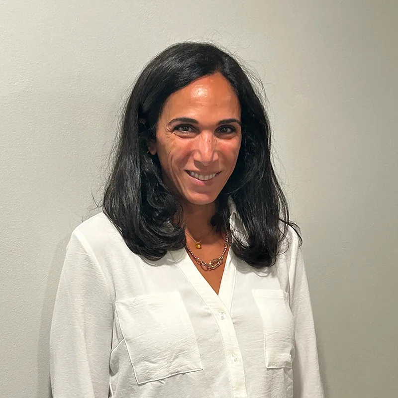 Woman with long black hair wearing a white shirt, smiling against a plain background.