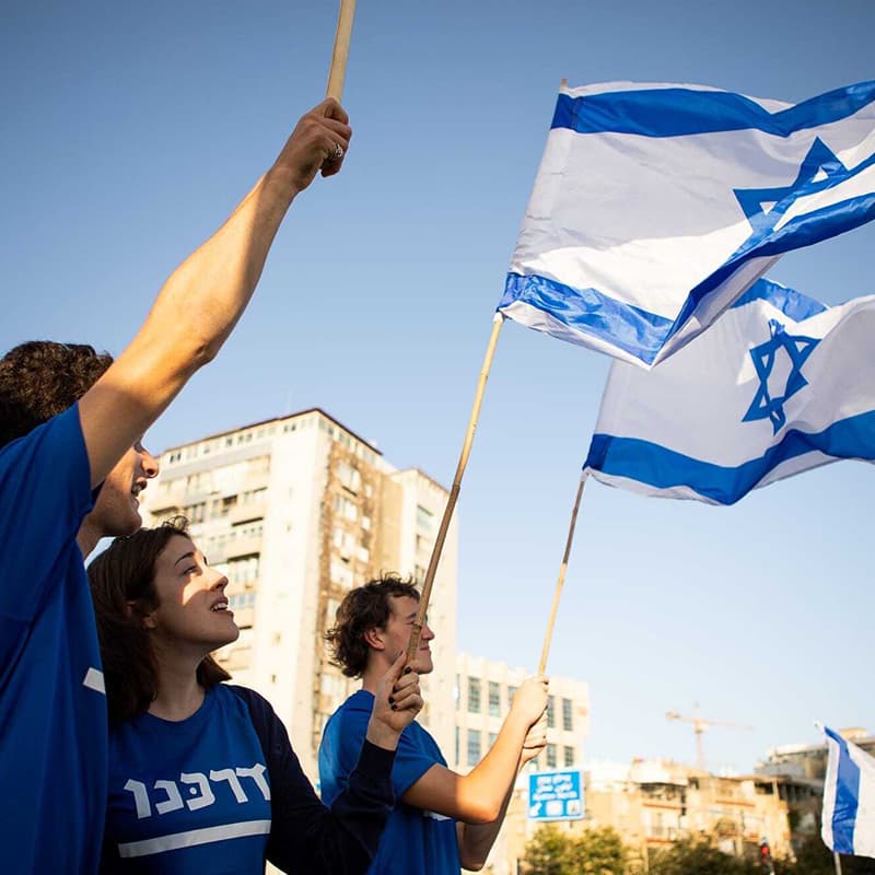 A young group of Israeli youth waving Israeli flags in the outdoor sun.
