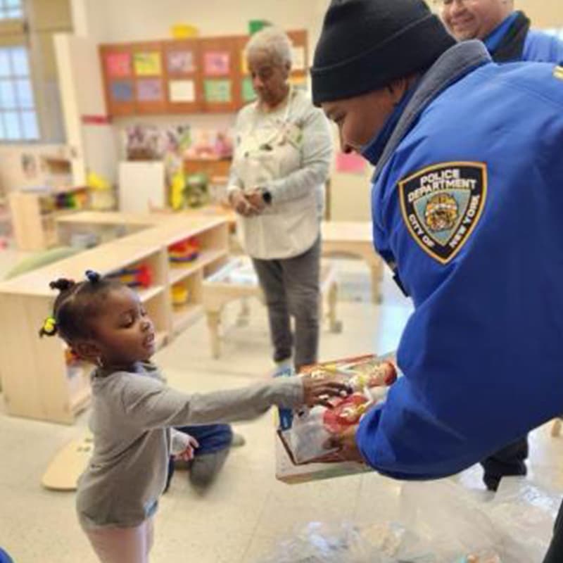 A police officer handing a toddler a toy in a classroom.