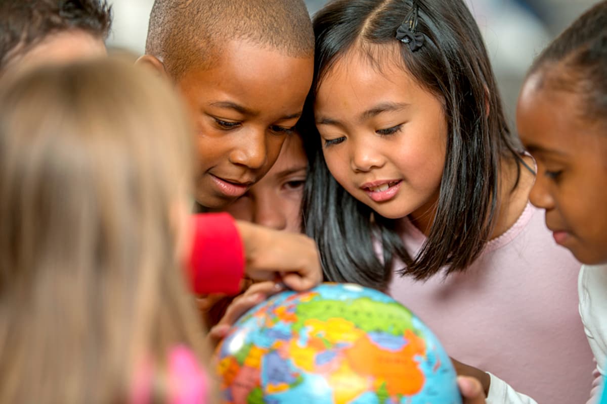 A diverse group of children pointing to a country on a globe.