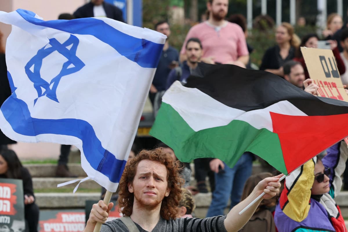 A man with long ginger hair waving a Palestinian and an Israeli flag.